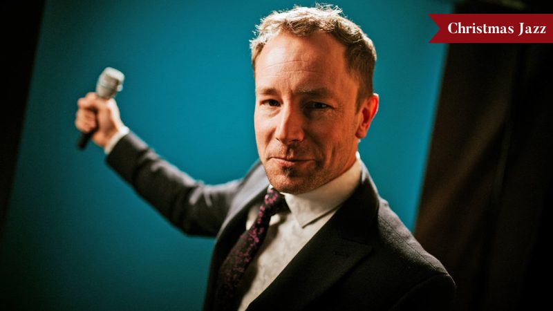 Singer Cormac Kenevey wearing a suit, holding a microphone in from of a blue and black backdrop.