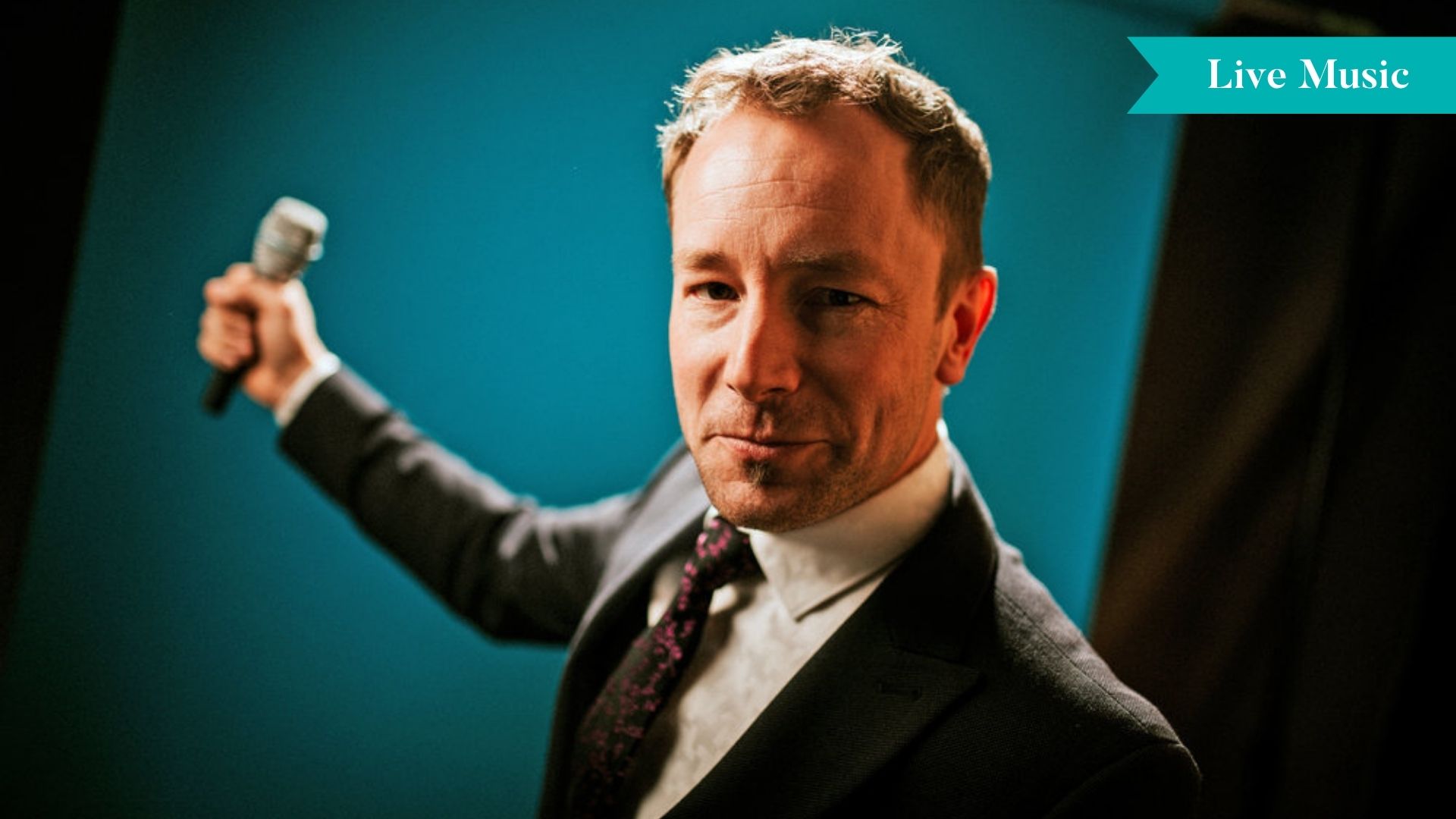 Singer Cormac Kenevey wearing a suit, holding a microphone in from of a blue and black backdrop.