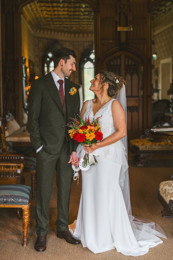 A wedding couple in 2025 gazes lovingly into each other’s eyes in an elegant drawing room, with floor-length antique mirrors reflecting the space behind them.